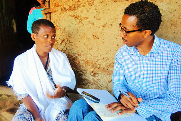 Male student on an international trip interviews a native woman as a child looks on.