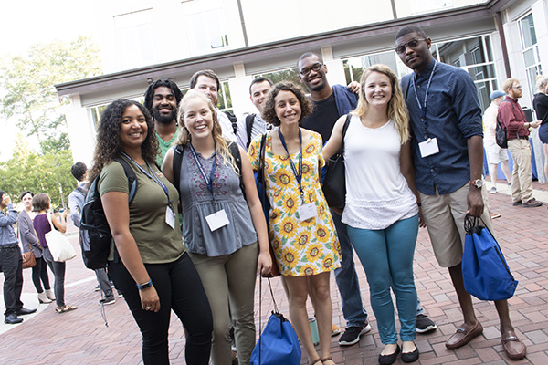 A group of nine diverse male and female students pose and smile during orientation.