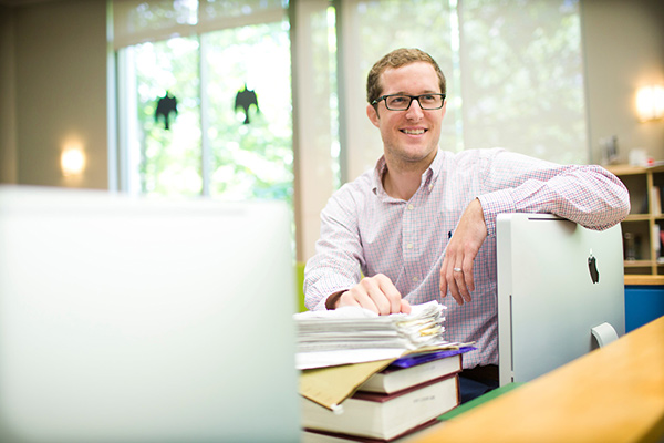 Male student sits alone and smiles as he leans on the computer monitor.