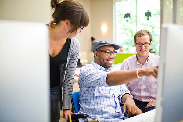 Three adults smile pleasantly at a computer screen while researching information.